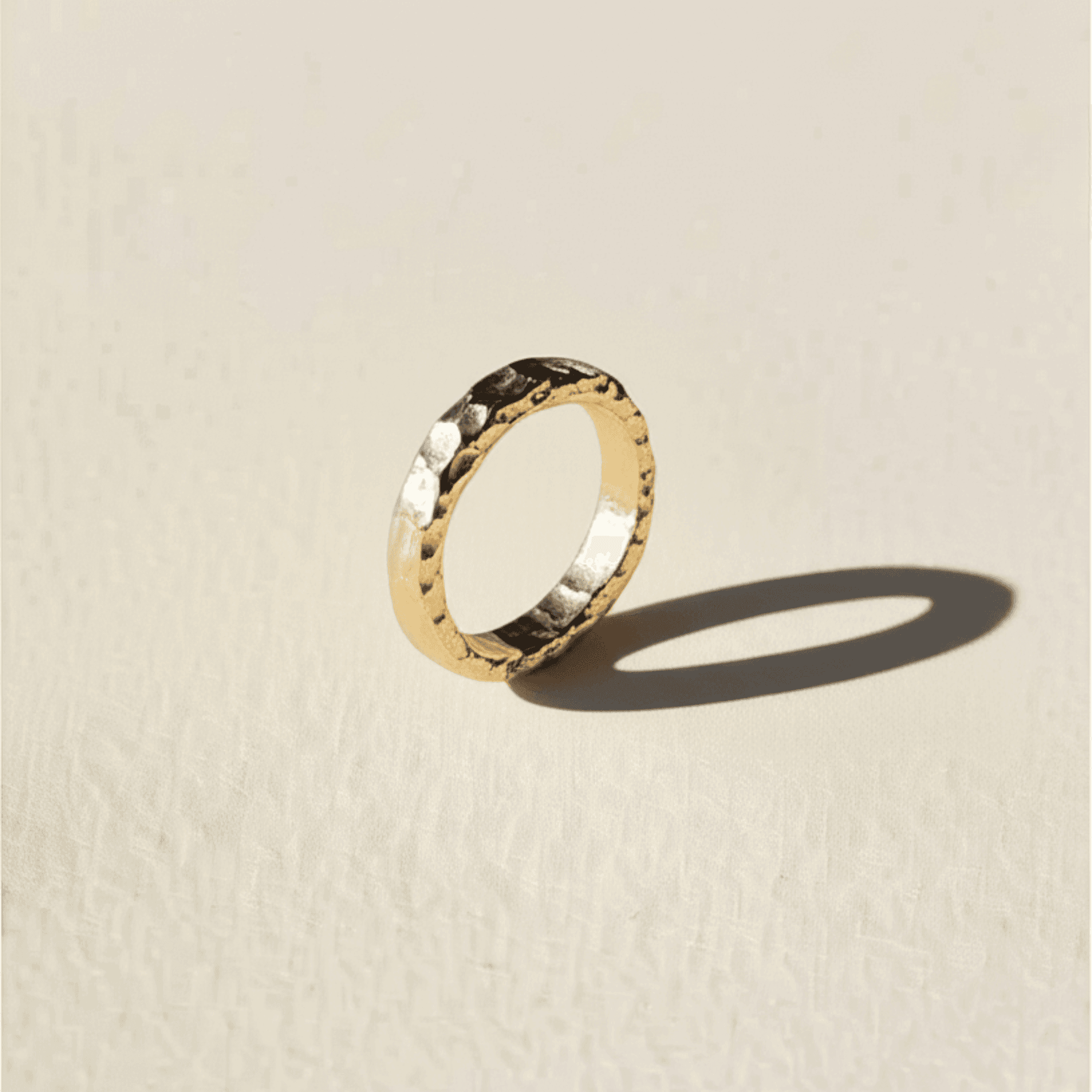 A hammered gold-colored band standing on a warm surface.